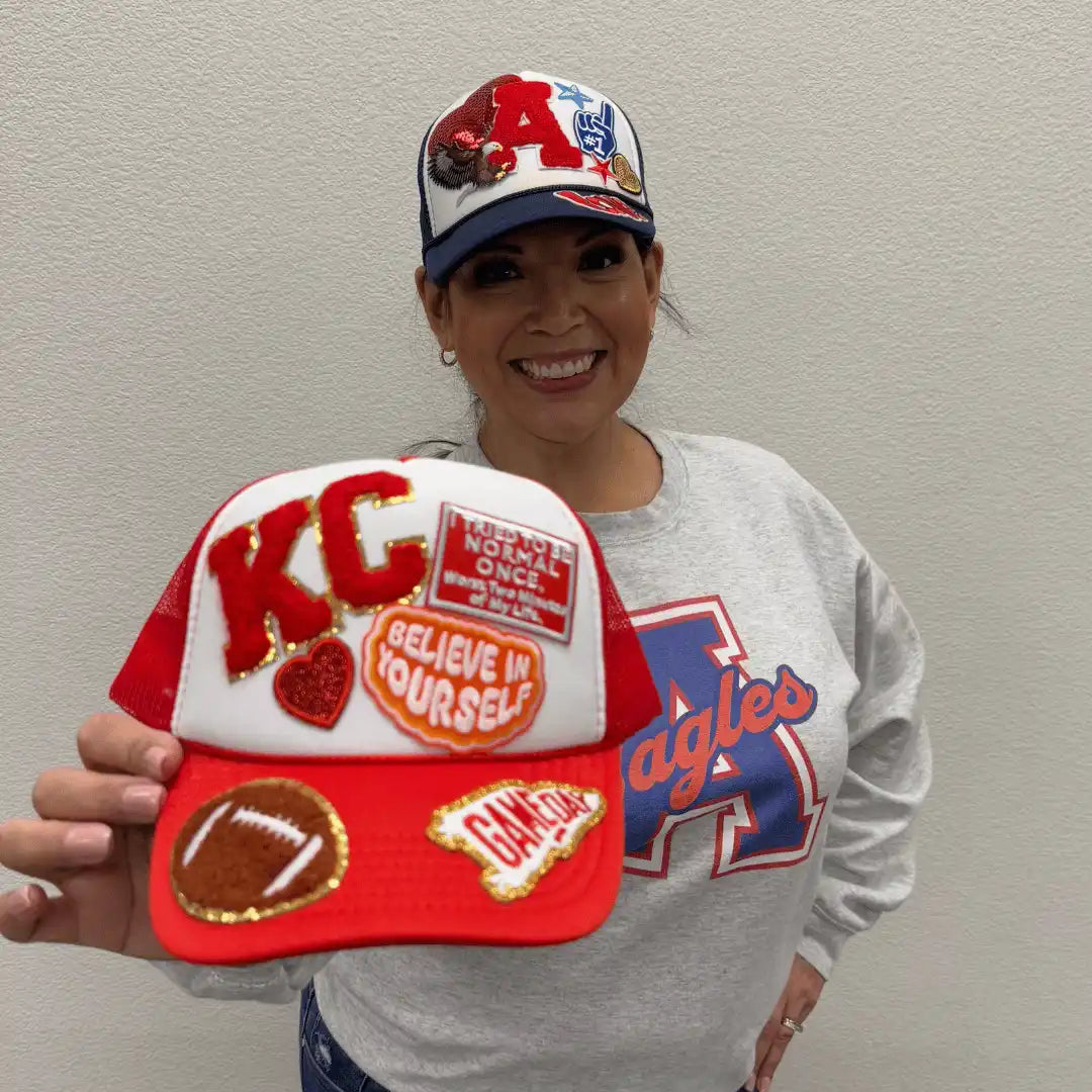 A woman proudly displaying two customized trucker hats.