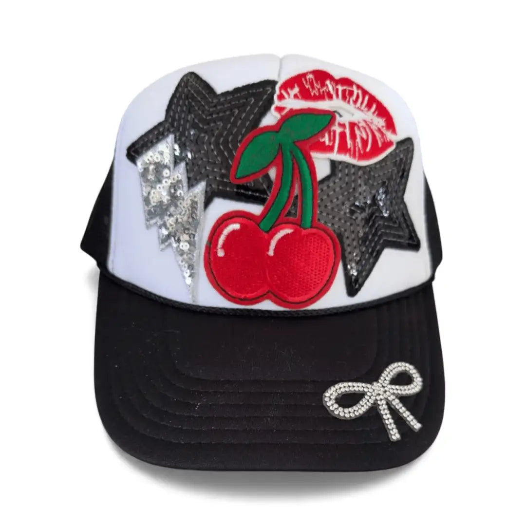 White and black trucker hat with cherry, star patches, rhinestone bow, sequins, mesh back, adjustable strap.