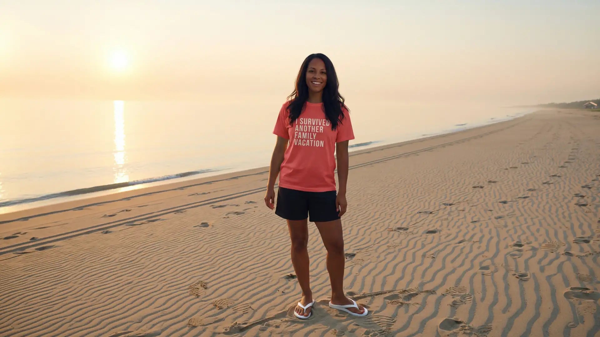 A woman wearing a coral-colored t-shirt with the text ’i survived another family vacation’ printed on it, paired with black shorts and white flip-flops.
